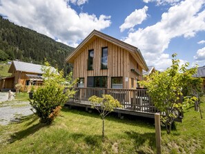 Un chalet en bois doté d’un balcon, entouré de verdure et avec une chaîne de montagnes en toile de fond.