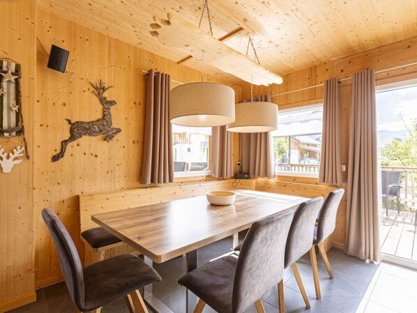 A wooden interior with a dining table, chairs, and a large window with curtains. - Superior Chalet With Whirlpool (Murau)