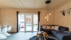 A modern living room with a wooden ceiling, a black leather sofa, a dining table with white chairs, and a glass door leading to an outdoor area. - Cosy Chalet With hot tub (Sankt Georgen am Kreischberg)