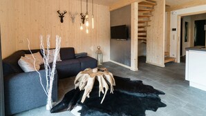 A modern living room with a dark grey sofa, wooden walls, a mounted TV, and a unique wooden table centerpiece. - Cosy Chalet With hot tub (Sankt Georgen am Kreischberg)