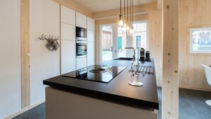 A modern kitchen with a central island, stainless steel appliances, and a hanging light fixture. - Cosy Chalet With hot tub (Sankt Georgen am Kreischberg)