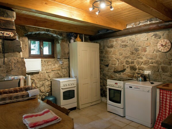 A rustic kitchen with stone walls, a wooden ceiling, and basic appliances including a stove, oven, and washing machine. - Secluded Stone Villa Retreat (Saint-Pierre-sur-Doux)