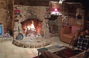 A stone fireplace with a fire, a television, and a cozy seating area with a chair and a small table.