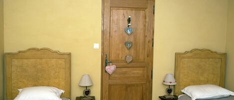 Une chambre avec deux lits, une porte en bois et une petite table avec une lampe.
