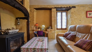 Een gezellige woonkamer met een leren bank, een tafel met een tafelkleed met bloemenprint, een houten stoel, een open haard en een raam met gordijnen.