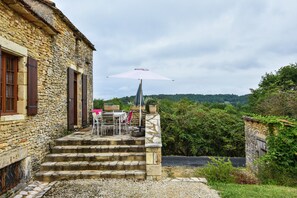 A stone building with a patio area featuring a table and chairs, an umbrella, and steps leading to the entrance. - Charming Family Retreat in Loubejac (Loubejac)