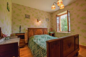 A room with a bed, wooden nightstands, a desk, and a window with a view of trees. - Charming Family Retreat in Loubejac (Loubejac)