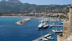 Un port de plaisance avec des bateaux amarrés, un mur de pierre et une chaîne de montagnes en arrière-plan.