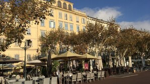Un café avec des tables en terrasse, un bâtiment doté de fenêtres en arc de cercle et un ciel dégagé.
