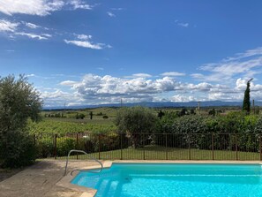 A swimming pool with a metal ladder, surrounded by a fence, and a view of a green landscape with hills and a clear sky. - Cosy Villa With Pool (Montbrun-des-Corbières)