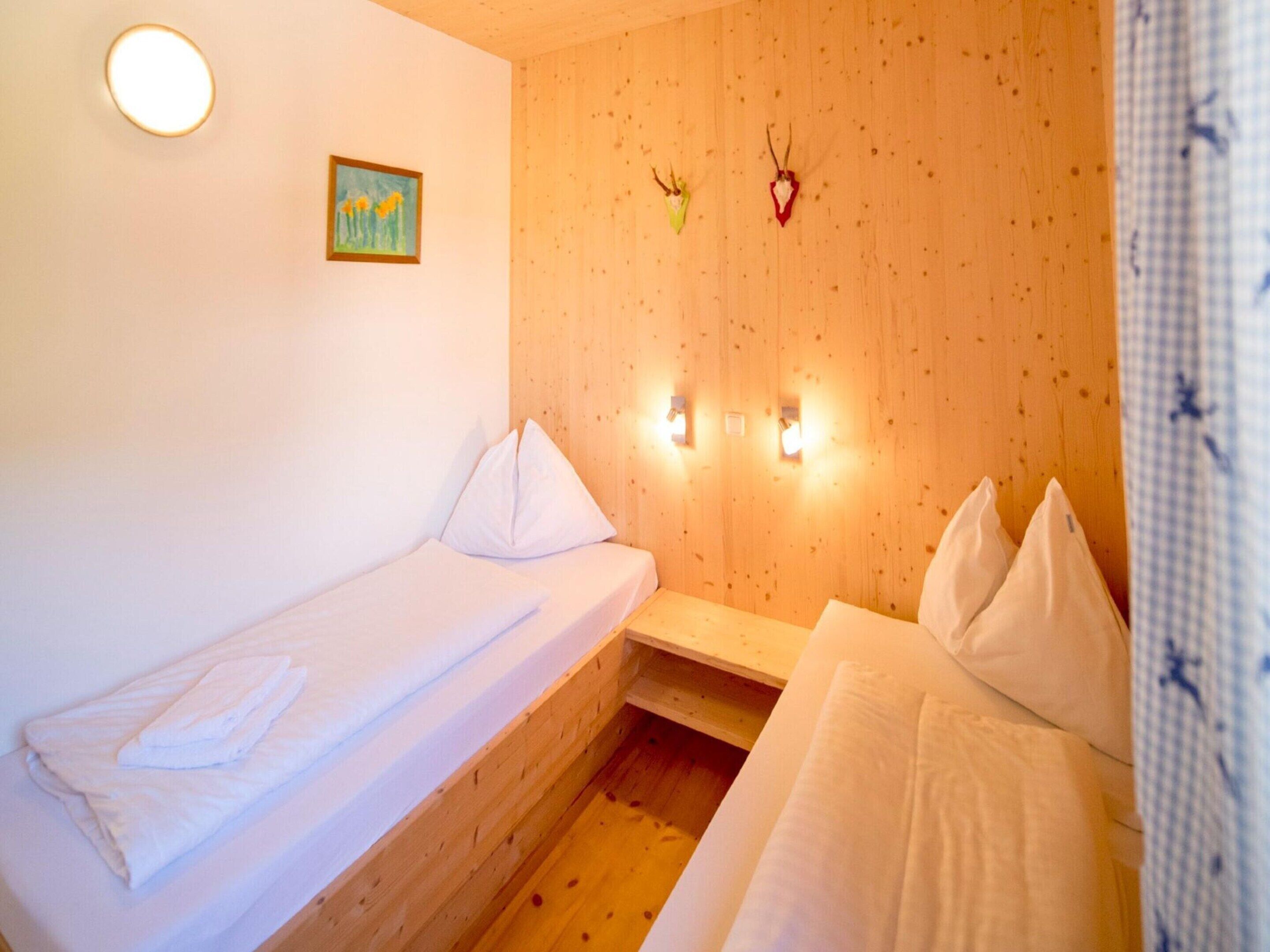 A small, cozy room with two beds, wooden walls, a painting, and wall-mounted lights.
