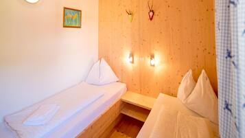 A small, cozy room with two beds, wooden walls, a painting, and wall-mounted lights.