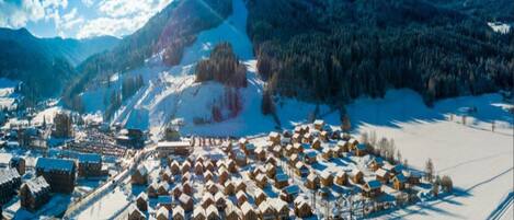 A snow-covered village with wooden houses arranged in a circular pattern, surrounded by mountains and a clear sky.