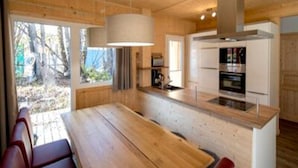 A modern kitchen with wooden cabinetry, a central island, and a dining area with red chairs. - Charming Chalet With Whirlpool (Sankt Georgen am Kreischberg)