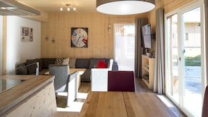 A modern living room with a wooden floor, a sofa, a dining table, and a large window with curtains. - Charming Chalet With Whirlpool (Sankt Georgen am Kreischberg)
