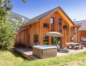 Una cabaña de madera con jacuzzi, mobiliario exterior y una terraza.