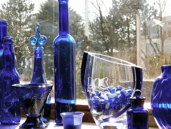 Eine Auswahl blauer Gläser auf einem Tisch nahe einem Fenster mit Blick auf Bäume.