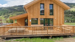Une cabane en bois dotée d’un balcon, de grandes fenêtres et offrant une vue sur une vallée verdoyante.