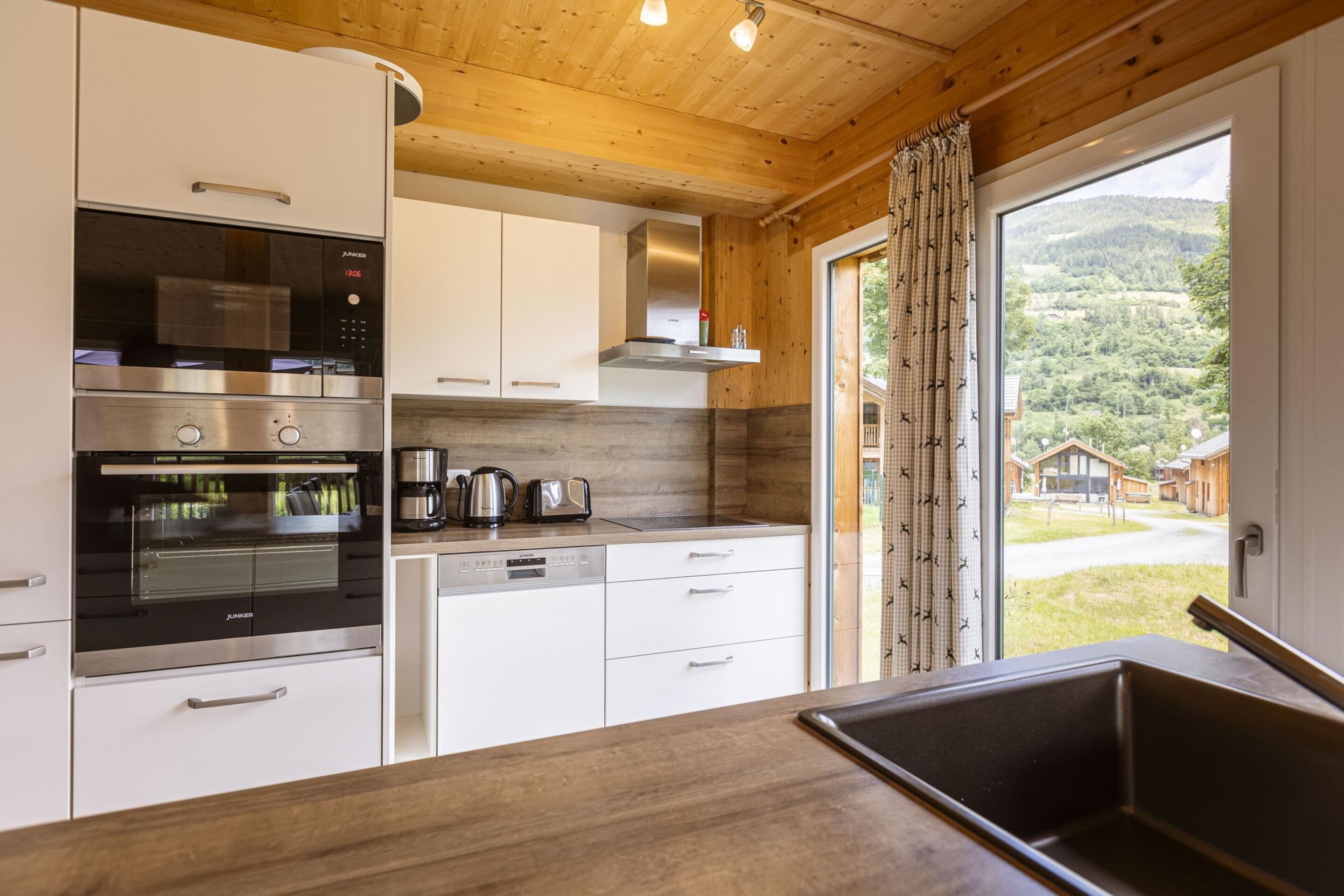 Eine moderne Küche mit Edelstahlgeräten, weißen Schränken und Blick auf eine gebirgige Landschaft durch ein großes Fenster.