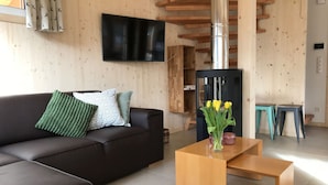 Un salon moderne avec un canapé foncé, une table basse en bois et un téléviseur à écran plat fixé au mur.