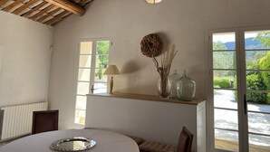 Une pièce avec un plafond en bois, un miroir rond, une lampe, un vase contenant des plantes séchées et une vue sur la verdure à l’extérieur.