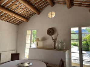 A room with a wooden ceiling, a round mirror, a lamp, a vase with dried plants, and a view of greenery outside. - Oppede Villa With Private Pool (Oppede)