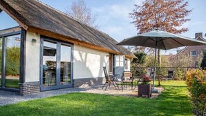 A modern house with a thatched roof, large glass windows, and a patio area with outdoor furniture. - Classy Holiday Home in Alphen With Garden (Alphen)