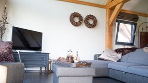 A modern living room with a sectional sofa, a flat-screen TV, and a decorative wall with two wreaths. - Classy Holiday Home in Alphen With Garden (Alphen)