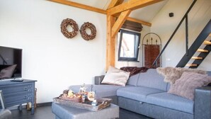 A living room with a grey sofa, a coffee table with snacks, a TV, and a staircase. - Classy Holiday Home in Alphen With Garden (Alphen)