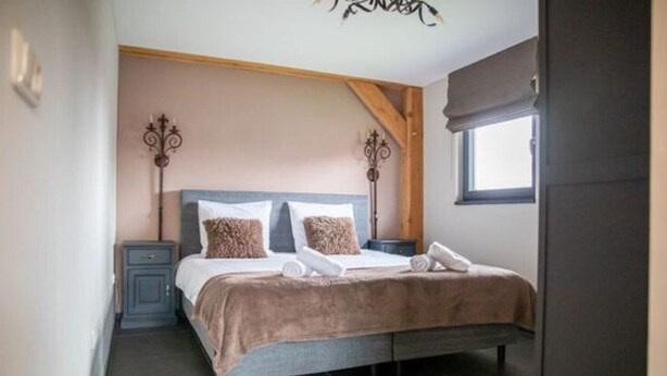 A bedroom with a bed, two bedside tables, a window with a blind, and a chandelier. - Classy Holiday Home in Alphen With Garden (Alphen)