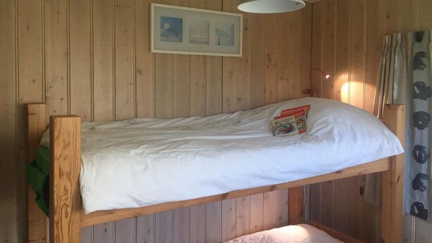 En køjeseng med hvid madras og en pude, en hængende metal lampe og et billede i ramme på væggen.