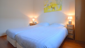 A double bed with white linens, two bedside tables with lamps, a wooden wardrobe, and a wall painting.