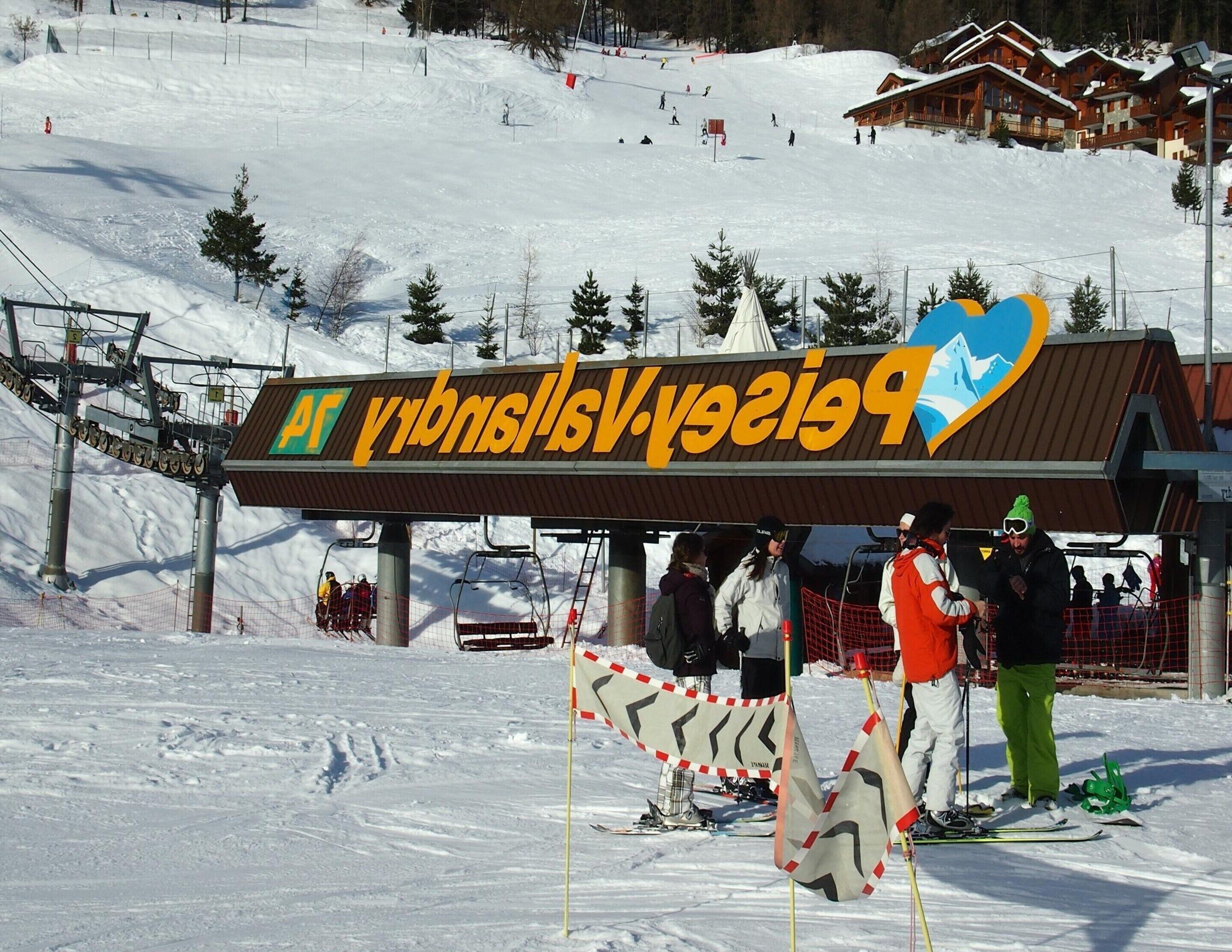 A ski resort sign with a mountain logo, ski lift, and a building with a ski lift in the background.