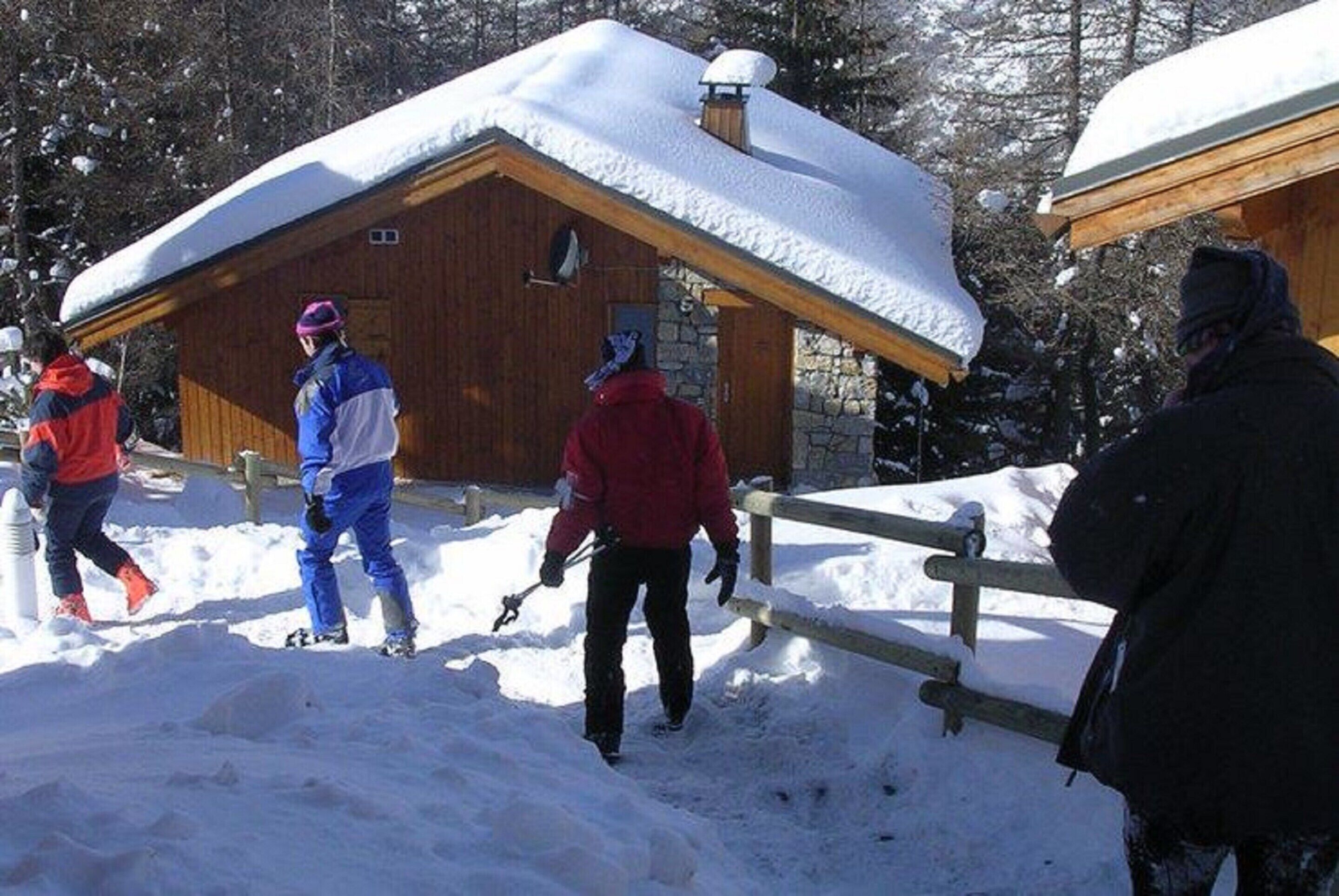 A wooden cabin with a snow-covered roof, surrounded by snow.