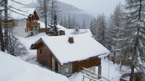 A wooden cabin with a stone foundation, surrounded by snow-covered trees and a mountainous backdrop. - Chalet in Vallandry Near Paradiski Ski Area (Landry)