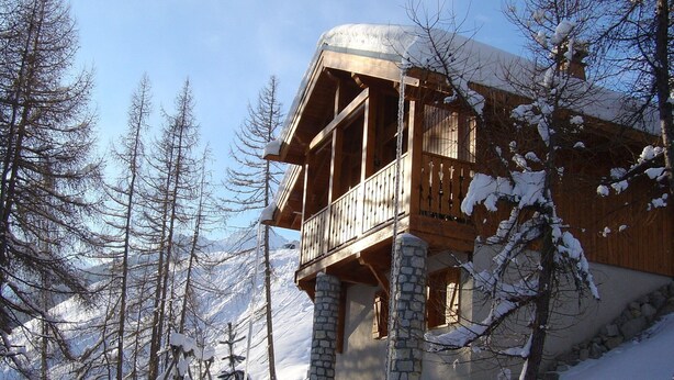 A wooden chalet with a balcony, stone foundation, and a snowy mountainous backdrop. - Chalet in Vallandry Near Paradiski Ski Area (Landry)