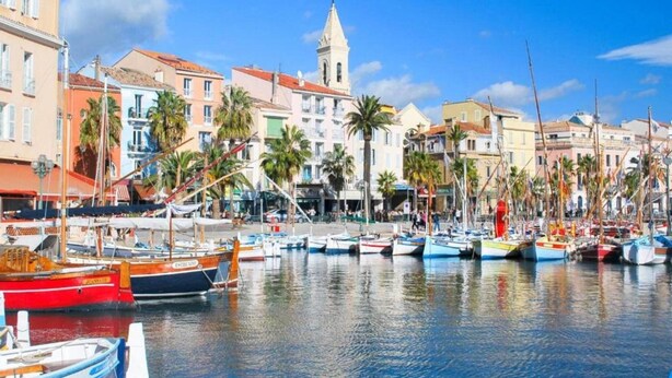 Un puerto deportivo con barcos amarrados, una iglesia con un campanario y edificios coloridos a lo largo del muelle.