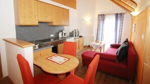 A compact kitchen with wooden cabinets, a granite countertop, and a dining area with red chairs.