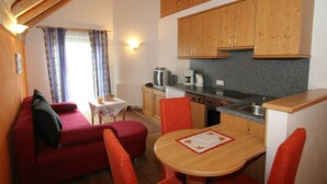 A cozy room with a red sofa, a small table, and a kitchen area with wooden cabinets and a stove.