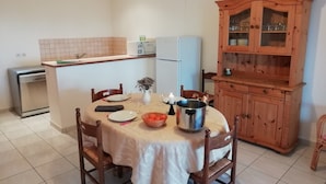 Een eethoek met een tafel gedekt voor twee personen, een keuken met een koelkast, en een houten kast met glazen deuren.