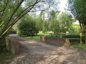 A gravel path leading through a wooded area with a wooden fence and a brick wall. - Holiday Home in Quend-plage Near the Sea (Quend)