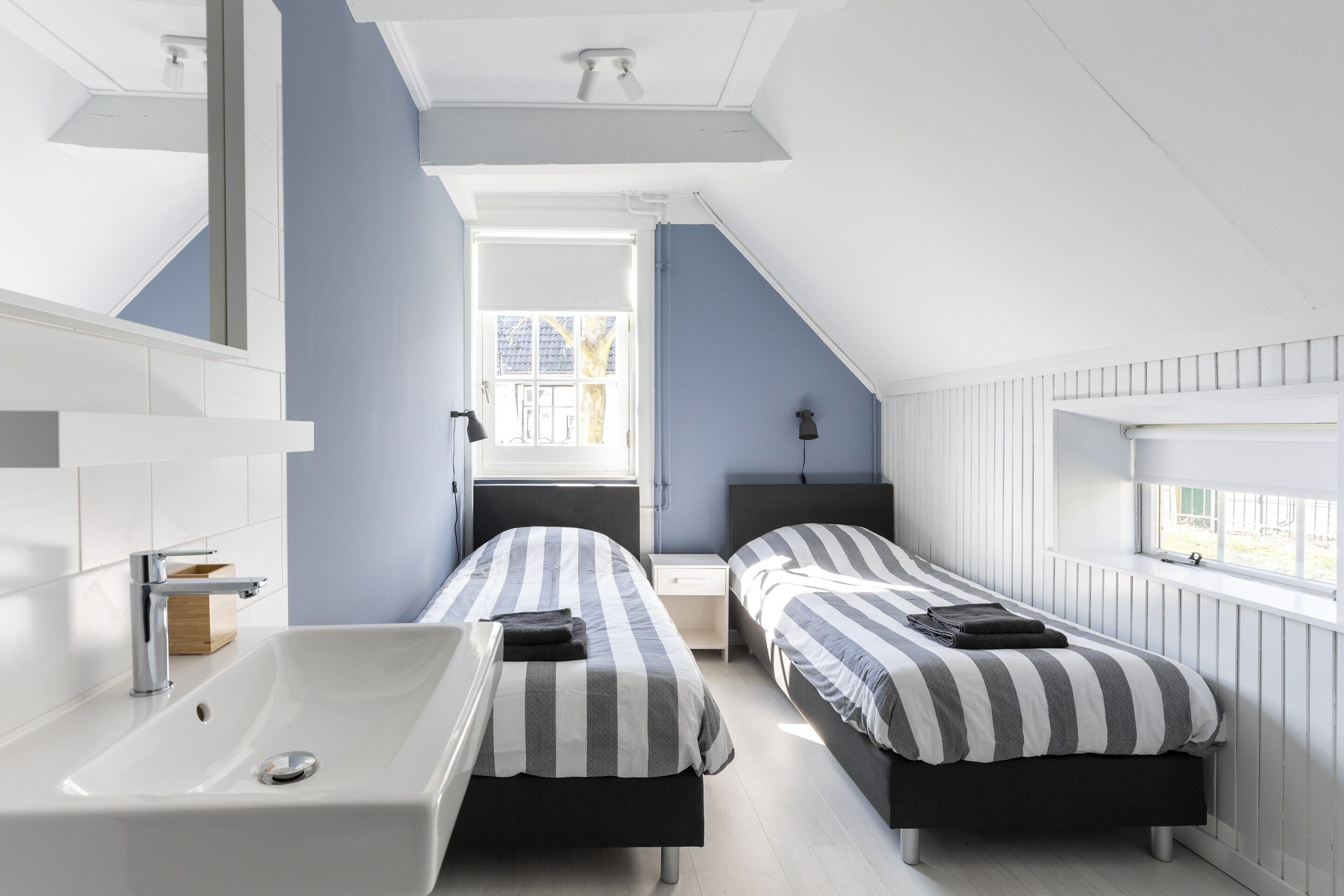 Une chambre moderne avec deux lits, une grande fenêtre et un lavabo blanc.