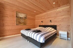 A modern bedroom with a wooden ceiling, a large bed with striped bedding, two bedside lamps, and a small bedside table.