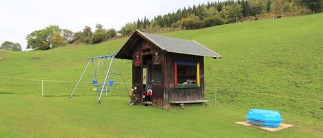 A rustic wooden cabin with a swing set and a blue container nearby.