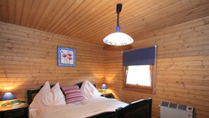 Een slaapkamer met houten lambrisering, een bed, bedlampjes, een raam met zonwering en een wandradiator.