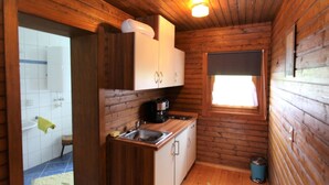 Een compact houten vakantiehuisje met een kitchenette, een klein raam en een deur naar een badkamer.