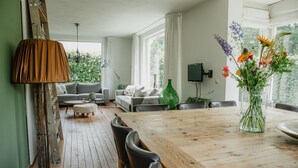 Ett rymligt vardagsrum med ett matbord i trä, två soffor och ett stort fönster med gardiner.