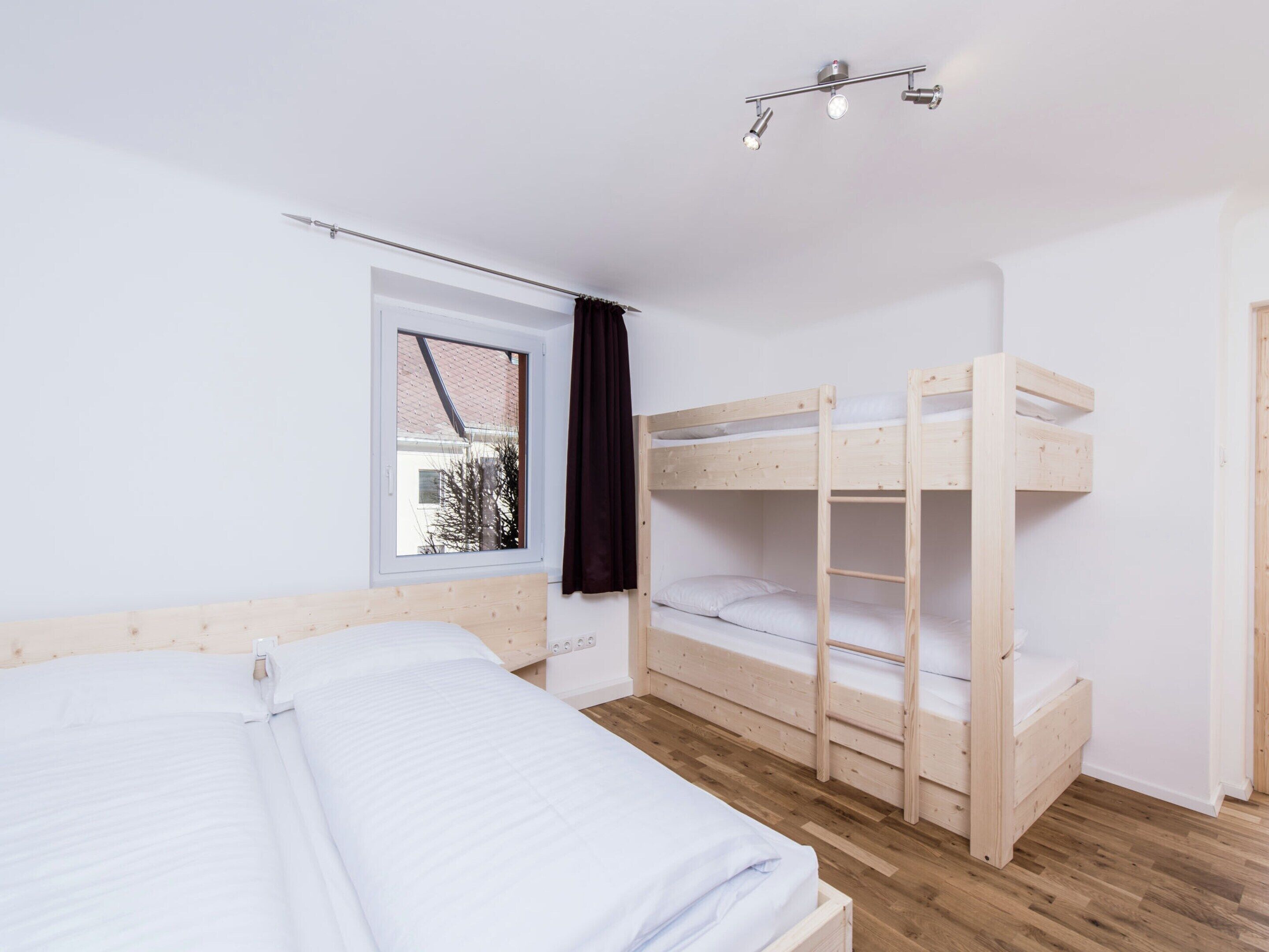 A room with a bunk bed, a single bed, a window with a view, and a ceiling light fixture.
