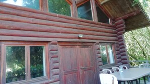 A log cabin with large windows, a wooden door, and a table with chairs outside. - Chalet in France Near the Beach & Pool (Quend)