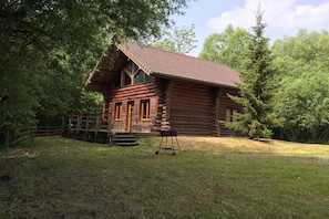A log cabin with a sloped roof, a front porch, and a small front yard.